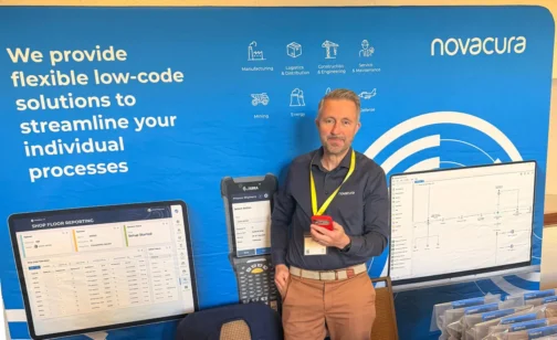 Man standing at a Novacura trade show booth, holding a smartphone and wearing a yellow lanyard, in front of a blue backdrop that reads “We provide flexible low-code solutions to streamline your individual processes.