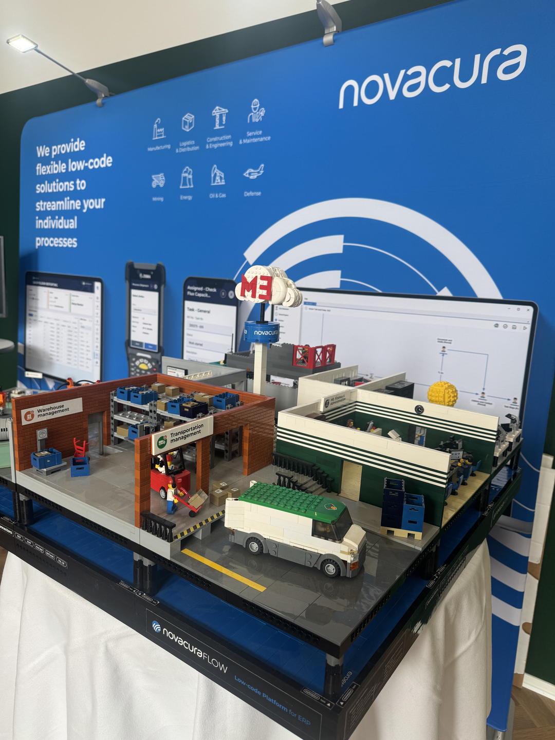 A custom LEGO diorama representing a Novacura Flow-powered industrial facility, displayed in front of a Novacura exhibition stand.