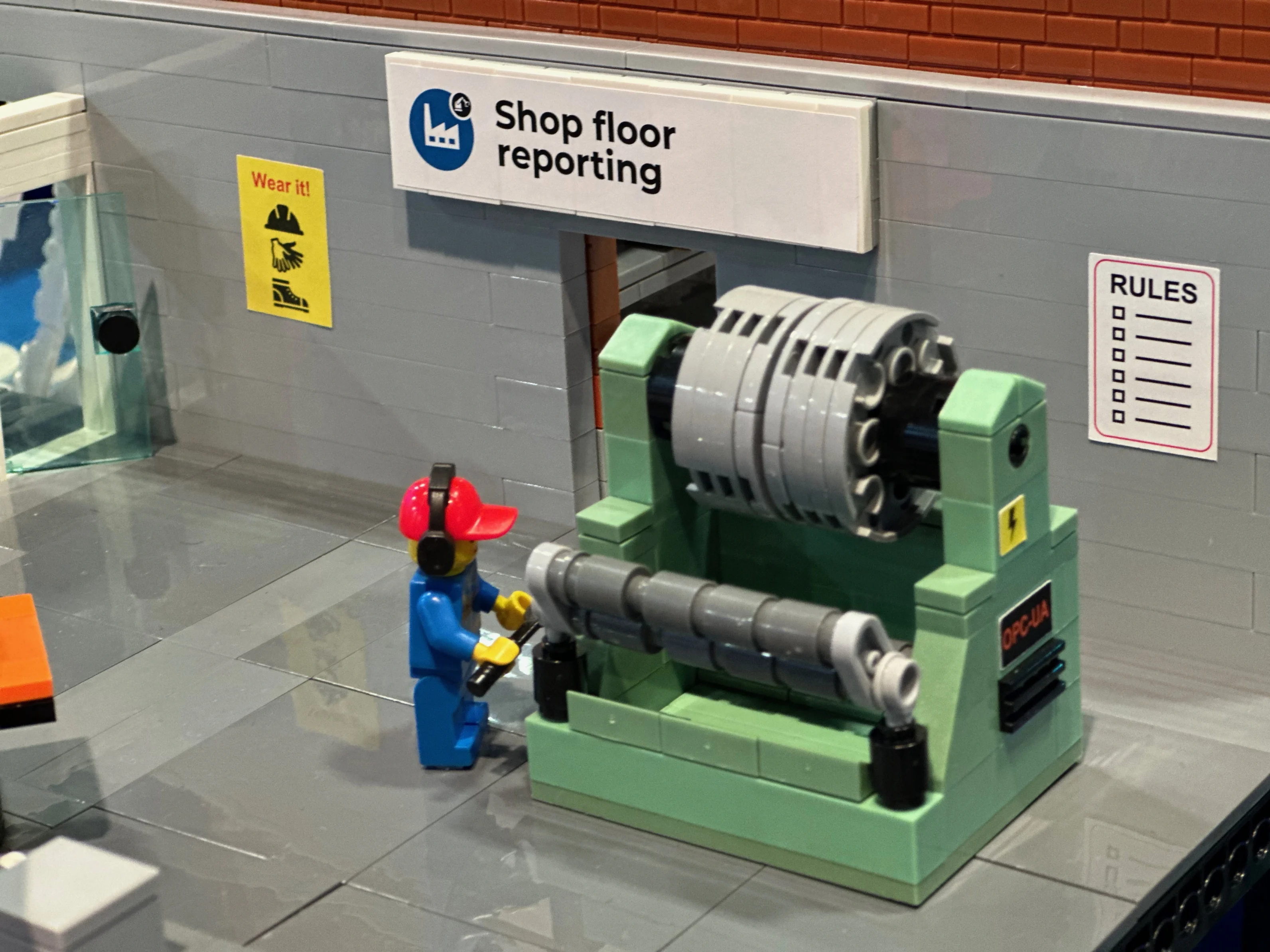 Close-up of a Lego worker minifigure operating factory machinery labeled Shop floor reporting and OPC-UA.