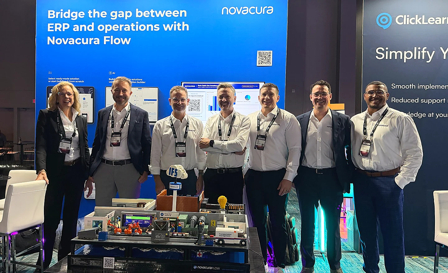 The Novacura team at the company’s IFS Unleashed 2026 booth, standing in front of a banner reading “Bridge the gap between ERP and operations with Novacura Flow”, with a Novacura Flow demo model on the table in front of them.